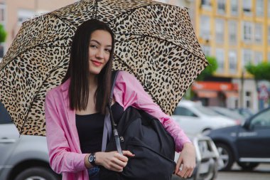 Sokakta şemsiyeli ve sırt çantalı genç bir kız.