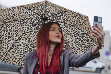 Yağmurda şemsiyeli kız cep telefonuyla öpücük yolluyor.