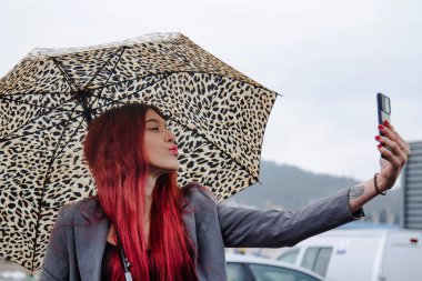 Yağmurda şemsiyeli kız cep telefonuyla öpücük yolluyor.