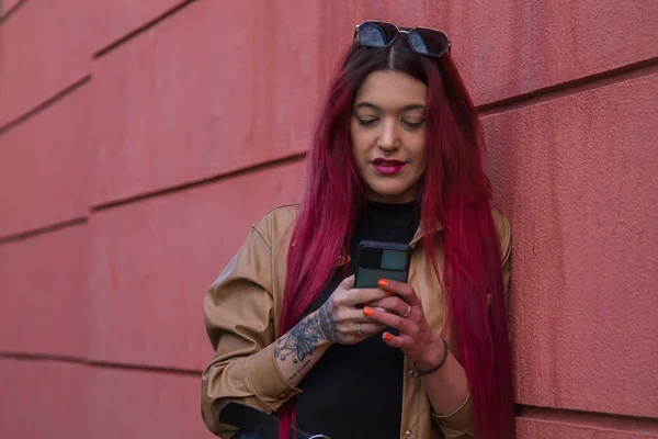 赤い背景に長い髪と携帯電話を持つ笑顔のファッションヒップスター女性 — ストック写真