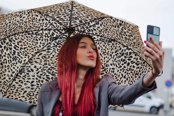 Yağmurda şemsiyeli kız cep telefonuyla öpücük yolluyor.