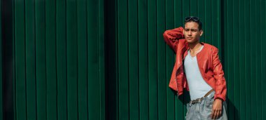 Latin kökenli genç adam yeşil duvarda poz veriyor.