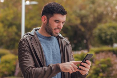 Genç adam sokakta telefonla konuşuyor.