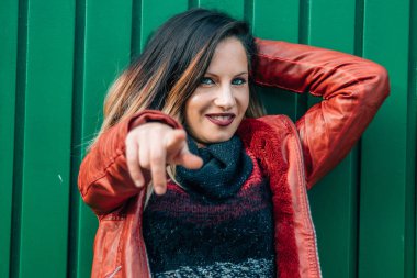 Duvarda deri ceketli genç bir kadın işaret ediyor.