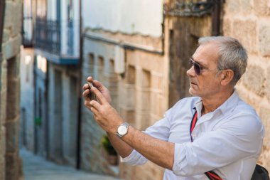 Şehirde cep telefonu olan orta yaşlı bir adam selfie mi çekiyor yoksa canlı video mu çekiyor?