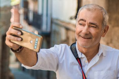 Şehirde cep telefonu olan orta yaşlı bir adam selfie mi çekiyor yoksa canlı video mu çekiyor?
