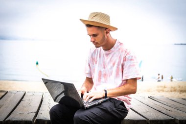 Kumsalda dizüstü bilgisayar kullanan genç bir adam.