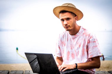 Kumsalda dizüstü bilgisayar kullanan genç bir adam.