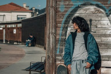 Latin kökenli genç kaykayıyla duvara yaslanıyor.