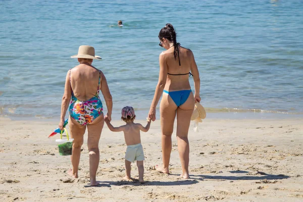 grandmother with daughter and grandson walking on the shore of the beach