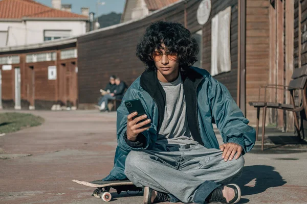 Giovane Seduto Sul Suo Skateboard Rilassato Consultando Suo Telefono Cellulare — Foto Stock