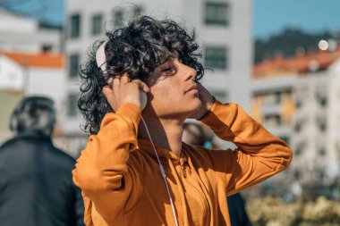 Latin kökenli rahat genç adam sokakta kulaklıkla müzik dinliyor.