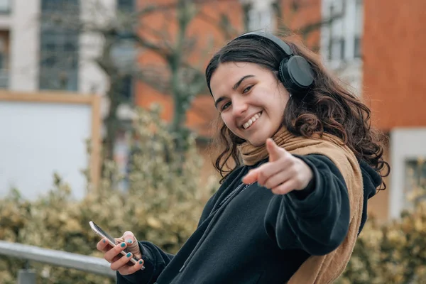 smiling girl with headphones in the street and pointing a direction