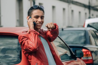 Gülümseyen genç adam cep telefonu ve işaret parmağıyla caddede