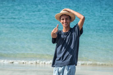 Plajda şapkalı genç Latin bir adam iyi bir jest yapıyor.