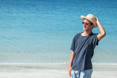 Plajda şapkalı ve güneş gözlüklü genç bir adamın portresi.