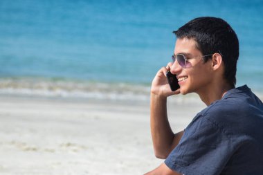 Genç adam sahilde cep telefonuyla konuşuyor.