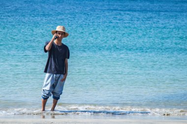 Genç adam sahilde ve telefonda konuşuyor.