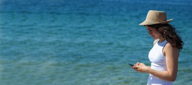 Kumsalda telefonla yürüyen rahat genç bir kadın.