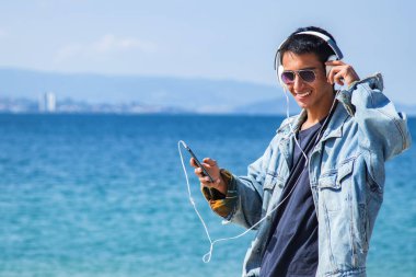 Sahilde yürüyen kulaklıklı genç adam.