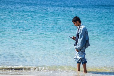 Plajda telefon ve kulaklıkları olan rahat bir adam.