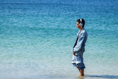 Plajda yürüyen kulaklıklı rahat bir adam.