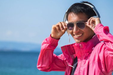 Dışarıda kulaklıklı mutlu genç bir adam var.