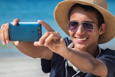 Genç adam sahilde telefonla selfie çekiyor.