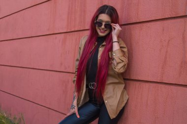 Duvarda güneş gözlüklü kızıl saçlı kadın poz veriyor.