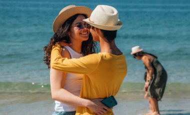 Düğün çifti sahilde mutlu bir şekilde sarılıyor.