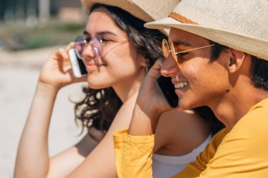 Kumsalda cep telefonuyla konuşan mutlu gençler.