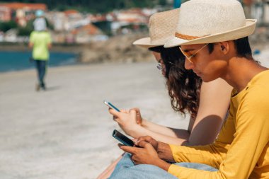 Plajda oturan gençler cep telefonu kullanıyorlar.