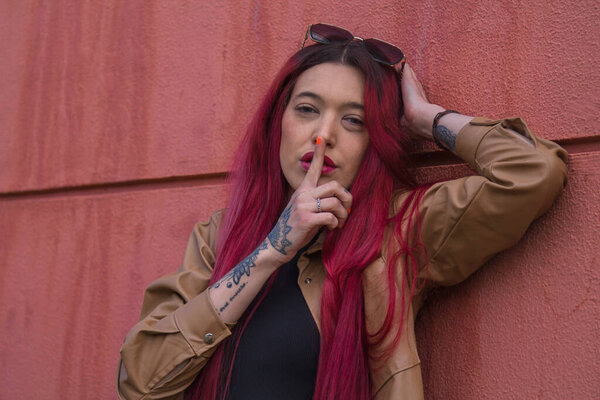 Молодая женщина делает знак молчания с пальцем на стене улицы