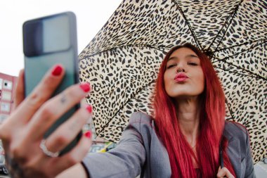 Yağmurda şemsiyeli kız cep telefonuyla öpücük yolluyor.