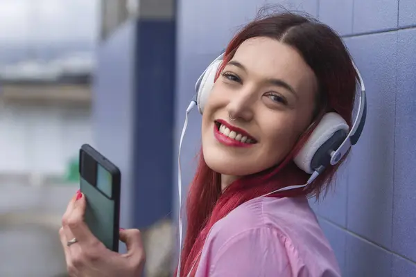 smiling young woman with headphones and phone on the street