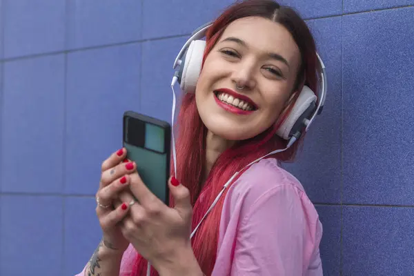 smiling young woman with headphones and phone on blue wall