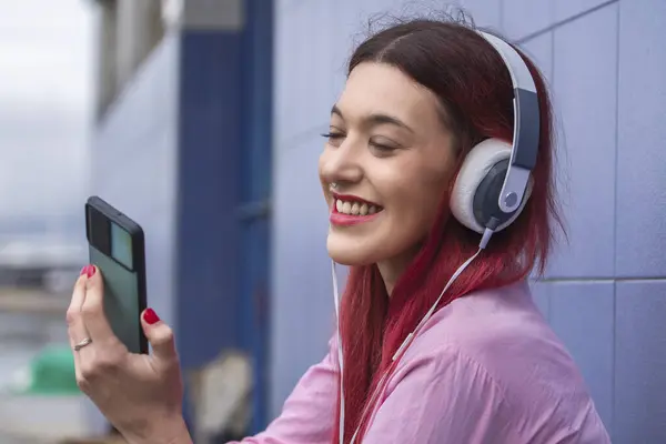 smiling young woman with headphones and phone on blue wall