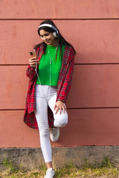 happy young woman with headphones and phone on the wall