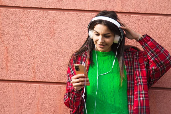 happy young woman with headphones and phone on the wall