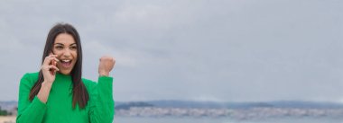 Dışarıda başarılı bir jesti ve akıllı telefonu olan mutlu genç bir kadın.