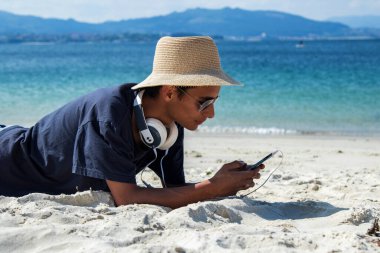 Kulaklıklı genç adam plajda dinleniyor.