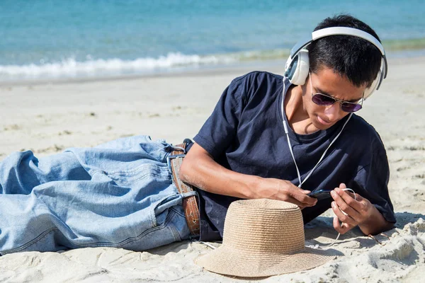 young man with headphones and phone relaxing on the beach