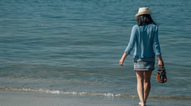 Rahatlamış genç bir kadın sahilde geziniyor.