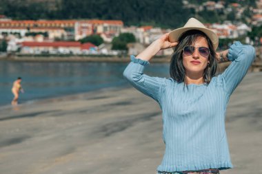 Şapkalı genç bir kadın kumsalda dinleniyor.