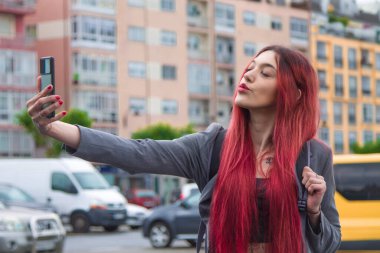 Genç bir kadın sokakta cep telefonuyla video ya da fotoğraf çekiyor.