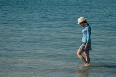 Rahatlamış genç bir kadın sahilde geziniyor.