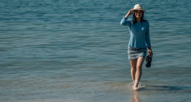 Çıplak ayaklı kadın sahilde tek başına yürüyor.