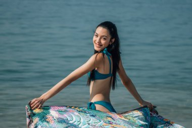 Bikinili rahat kadın ve çiçekli pareo sahilde eğleniyor.