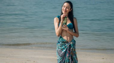 Neşeli kadın meyve suyundan zevk alıyor ve sahilde kendi portresini çekiyor.