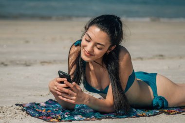 Plajda cep telefonuyla rahatlamış genç bir kadın.